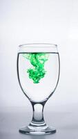 Transparent glass with green colored water isolated on white background photo