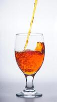 Orange colored water poured into glass isolated on white background photo