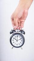 Hand holding classic black alarm clock isolated on white background photo
