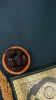 Muslim decoration with holy Quran and dates fruit for Ramadan and Eid al-Fitr isolated on dark green fabric background photo