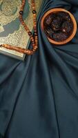 Muslim decoration with holy Quran, prayer beads, and dates fruit for Ramadan and Eid al-Fitr isolated on dark green fabric background photo