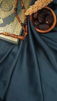 Muslim decoration with holy Quran, prayer beads, and dates fruit for Eid al-Fitr and Ramadan isolated on dark green fabric background photo