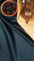 Muslim decoration with islamic lantern, dates fruit, and beige fabric for Ramadan and Eid al-Fitr isolated on dark green fabric background photo