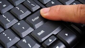 Close up on finger pressing enter button on keyboard isolated on black background photo