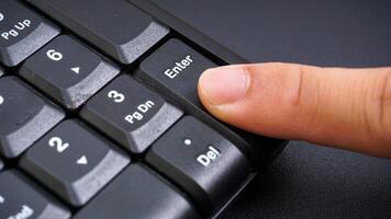 Close up on finger press enter button on computer keyboard isolated on black background photo