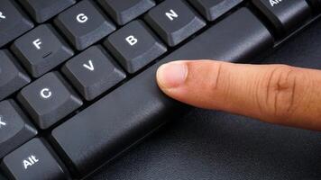 Close up on finger pressing space button on a computer keyboard isolated on black background photo
