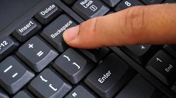 Close up on finger pressing backspace button on keyboard isolated on black background photo