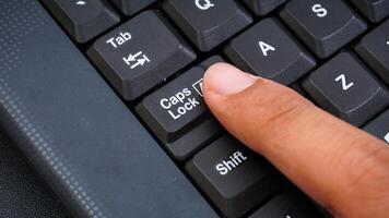 Close up on finger pressing caps lock button on keyboard isolated on black background photo