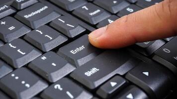 Close up on finger pressing enter button on a computer keyboard isolated on black background photo