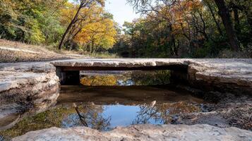 Autumn foliage reflected in a stream under a stone bridge photo