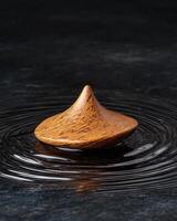 Wooden spinning top on a dark surface with water ripples photo