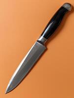 A sharp kitchen knife with a black handle on an orange background photo