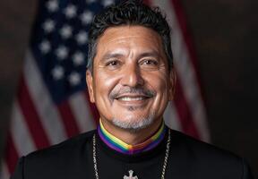 A portrait of a person wearing a rainbow stole in front of an American flag photo