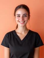 A young smiling woman in a black blouse poses confidently in front of a warm orange studio background conveying a professional and personable demeanor as the manager of a salon photo
