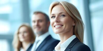 A group of professional business people including a smiling blond woman stand together in a modern office with large in the background photo
