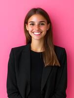 Portrait of a confident professional young woman with a warm friendly smile dressed in a black jacket and posing against a vibrant pink background photo