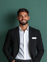 Portrait of a young smiling man in a suit standing at the hotel front desk and welcoming guests with a friendly expression photo