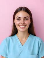 Portrait of a young smiling woman wearing a turquoise medical uniform or scrubs standing against a vibrant pink background and expressing a warm friendly demeanor photo