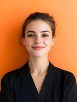 Portrait of a confident and enthusiastic young woman with a warm smile and natural makeup posing against an vibrant orange background photo