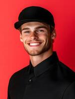 Portrait of a cheerful and friendly young man wearing a black uniform and cap smiling confidently against a bright red background photo