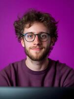 Portrait of a young smiling man with curly hair and glasses dressed casually and looking directly at the against a vibrant purple background suggesting his career as a game writer or developer photo