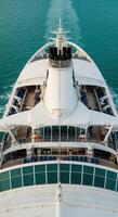 A luxury cruise ship sails on the turquoise sea, its wake trailing behind it. photo