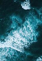 Overhead view of deep turquoise ocean water and foamy waves, creating abstract patterns. photo