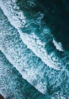 Mesmerizing aerial shot capturing the rhythmic dance of ocean waves crashing to shore. photo