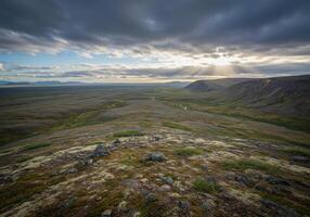 A wide view of a dramatic landscape with sun rays piercing through dark clouds over the distant mountains photo