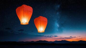 Two Illuminated Sky Lanterns Ascending Against a Starry Night Sky over Silhouetted Mountains photo