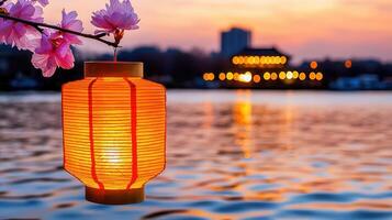 Illuminated Paper Lantern Hanging from Blossom Branch at Sunset Over Water photo