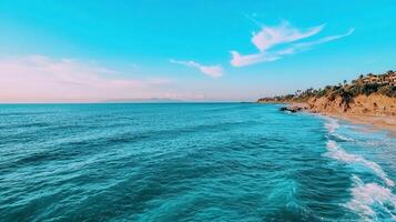 Serene Ocean Waves Crashing on Sandy Shore with Lush Green Coastline under a Vivid Blue Sky photo