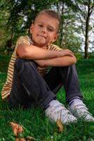 View of a schoolboy in a striped T-shirt sitting on the grass in the park photo