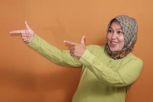 Smiling Muslim woman pointing with both hands playfully in studio, positive gesture stock photo for communication or promotion concept