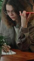 Vertical . Employee listens to voice message with comments from employer using phone, writes notes. Remote work. video