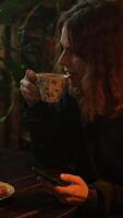 verticale . du quotidien routine, thé Pause. femme en utilisant téléphone intelligent séance à table avec tasse de thé dans confortable chambre. video