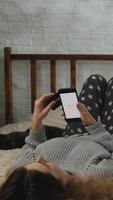 Vertical . Online checkout. Woman making online payments with smartphone and plastic bank card while relaxing in bed at home video