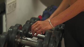 Close-up of hands selecting dumbbells from rack in gym for strength workout video