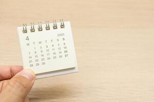 Hand holding mini Calendar for APRIL 2025 background. Calendar concept with 2025 APR calendar on wooden background. Copy Space for text. photo