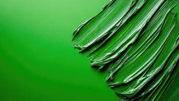 Thick glossy green paint is creating dynamic diagonal lines on matching green background with copy space photo