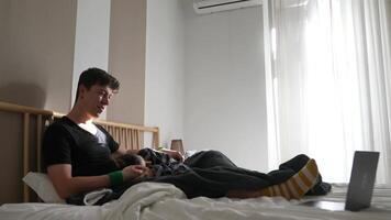 A young man relaxes at home on his bed, using his laptop and enjoying his leisure time video