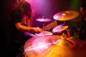 Drummer performing energetically with colorful stage lights illuminating the venue photo