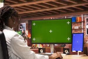 Woman browsing social media at home using green screen computer display and mockup tablet. Person talking with friends on social network online website using chroma key PC and isolated screen device photo