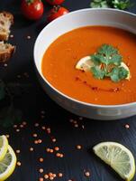 Delicious bowl of red lentil soup garnished with lemon and cilantro on a dark table photo