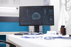 Computer screen in medical office shows neurological imaging of female brain and body. Vacant doctors workspace is arranged with diagnostic tools, files, and desktop pc displaying radiology results. photo
