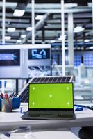 Green screen laptop on desk in industrial factory workspace featuring robotics, automation, and solar panel technology. Mockup notebook in photovoltaics factory used for analyzing data photo