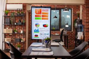 Vacant startup office with digital screen and chairs organized for company discussions. Technology and financial documents well arranged in brick wall workspace, ready for group meeting use. photo