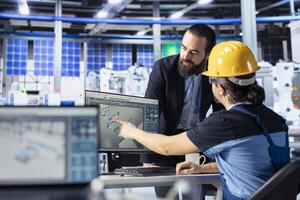 Photovoltaics factory engineer pointing to screen, showing manager ways to optimize production flow. Solar panels plant employee presenting team leader manufacturing process on computer display photo
