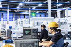 Photovoltaics factory employee programming solar manufacturing machinery using PC, finetuning system settings for maximum efficiency. Technician doing solar panel assembly job photo