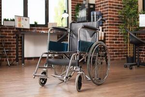 Closeup of wheelchair placed in middle of vacant workspace, with computer and business documents on desk in background. Shelves and plants complementing the spacious, organized brick wall office. photo